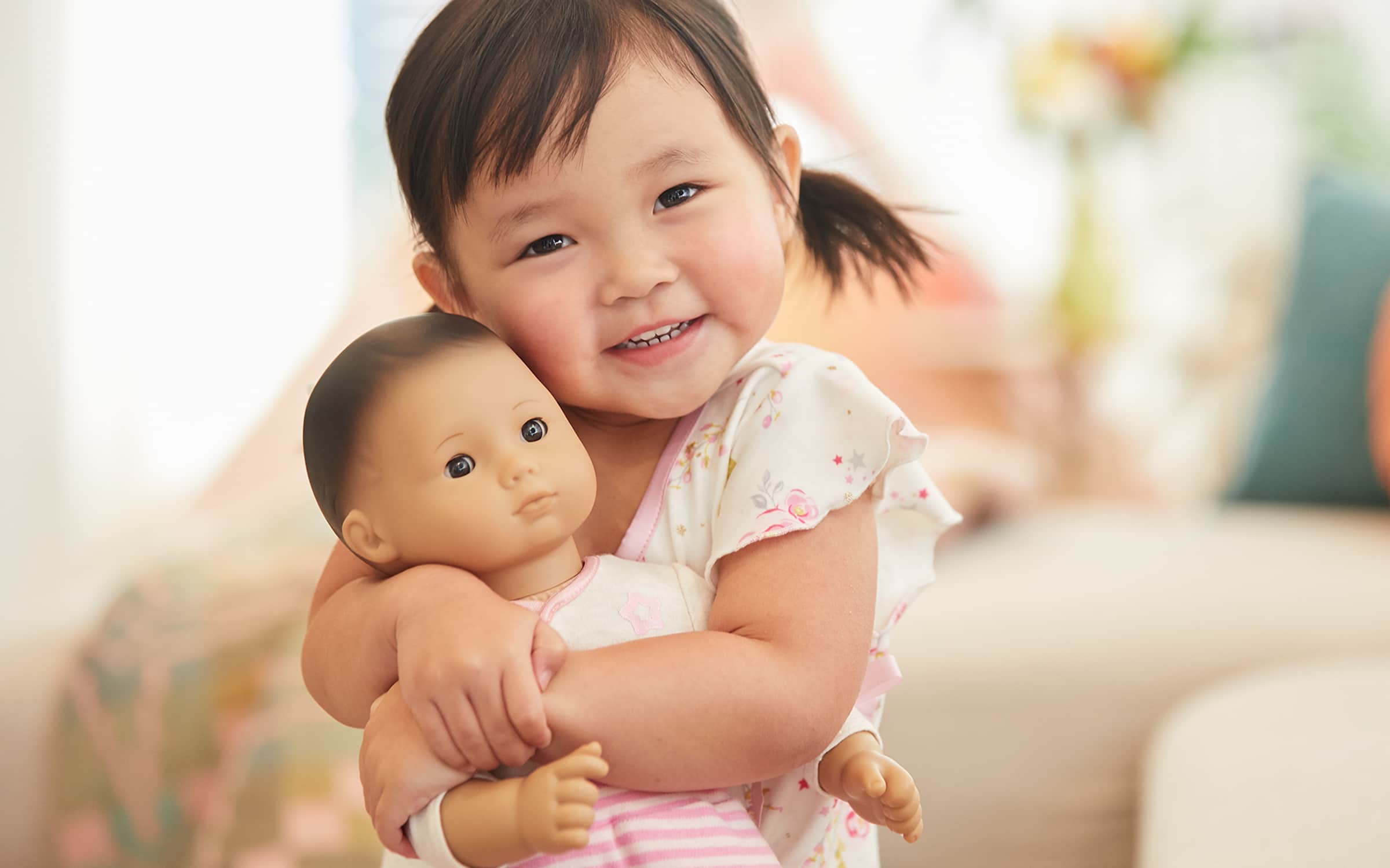 Image of little girl smiling and hugging a Bitty Baby doll
